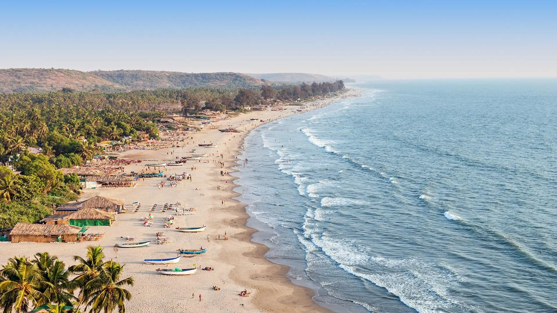 A bustling beach scene filled with people enjoying the sun and several boats anchored along the shore.