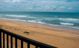 A scenic view of the beach from a balcony, showcasing golden sands and gentle waves under a clear blue sky.