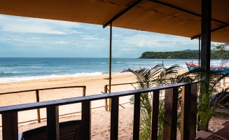 A scenic view of the beach from a balcony, showcasing golden sands and gentle waves under a clear blue sky.