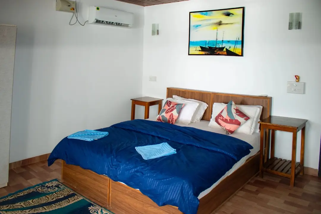 A neatly made bed with blue sheets, complemented by a decorative painting hanging on the wall above it.